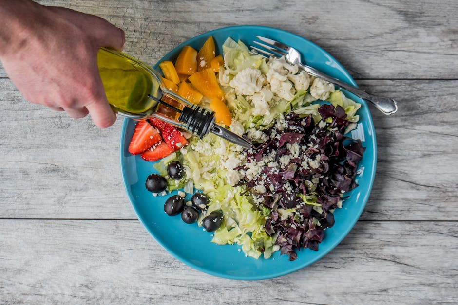 A vibrant vegetable salad with olives, feta, and strawberries being drizzled with olive oil.