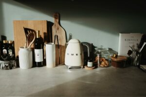 Various glass and ceramic bowls stylish electric kettle cutting boards and kitchen utensils locating on stone counter against gray wall in cozy kitchen